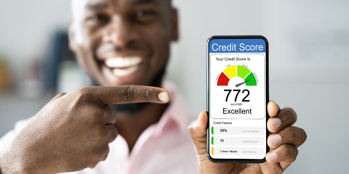 A man smiling and pointing at a smartphone displaying a credit score of 772, labeled as "Excellent."