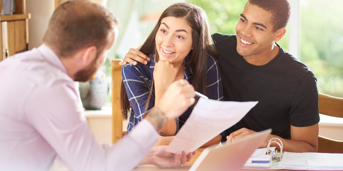 Smiling couple sitting with a financial advisor while reviewing mortgage documents.