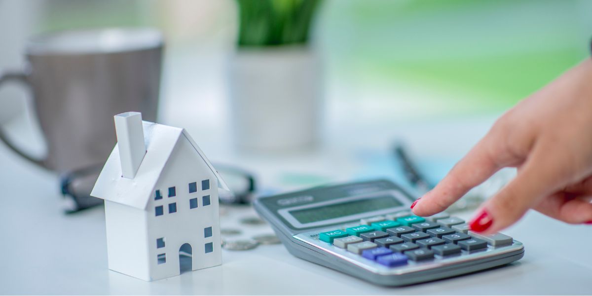 Person using a calculator with a small paper house model on the table.