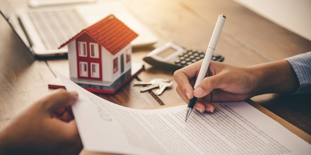 Person signing a mortgage pre-approval
with a small house model, keys, and calculator on the table